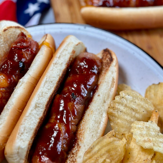 plate of bacon wrapped cheese stuffed hot dogs with chips