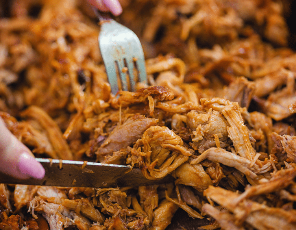 pile of pulled pork on a cutting board with a knife and a fork